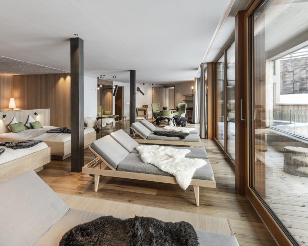 Sala relax con lettini imbottiti, pavimento in legno e grandi vetrate panoramiche