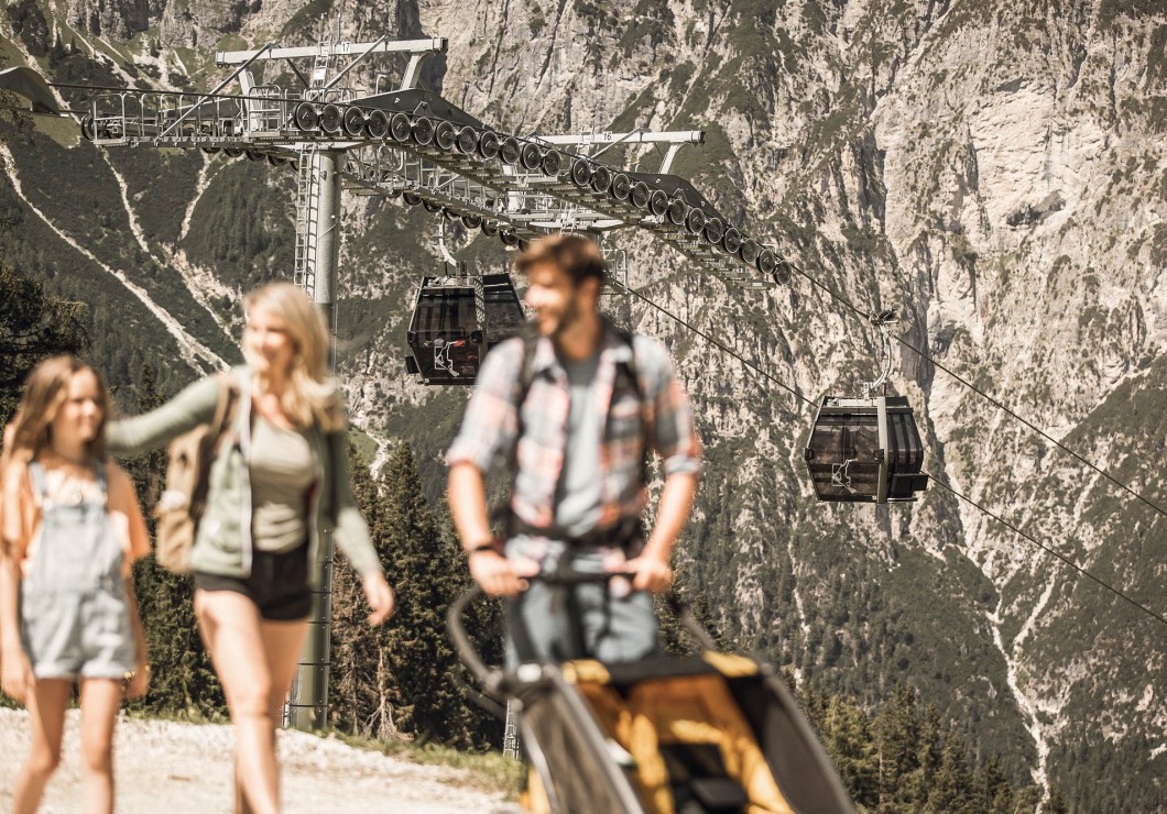 Ein Mann, eine Frau und ein Kind beim wandern, dahinter sind die Gondeln zu sehen von Ladurns