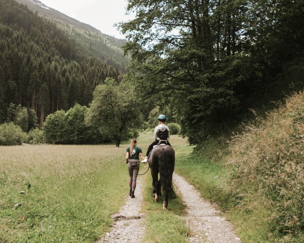 Ein Kind reitet mit einer Reitlehrerin im Wald in einer Kinderhotel Südtirols.