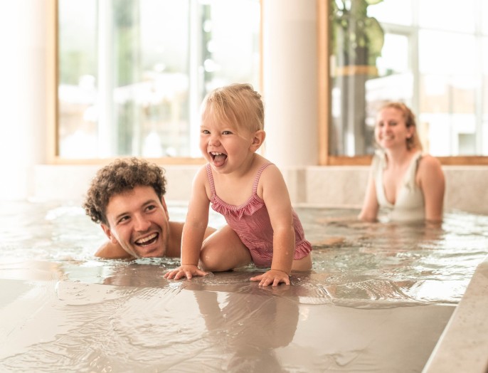 A daughter is playing with her family in the kiddie pool at the family hotel in South Tyrol with a water slide