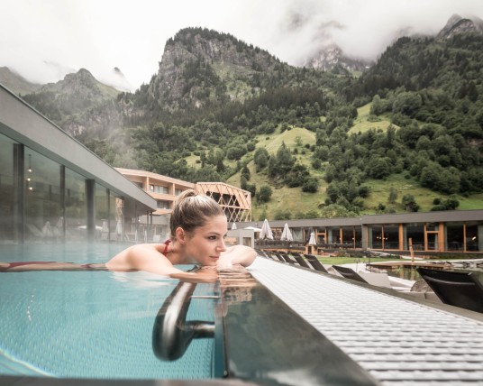 A woman is enjoying the outdoor infinity pool at a family hotel with a water slide in South Tyrol.