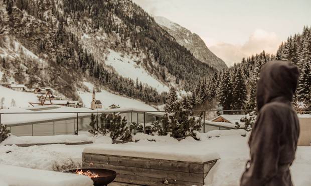 Ein Erwachsener steht auf der Terrasse des Adults Only Spa bereichs und genießt an der Feuerschale den wunderbachen Ausblick in die Winterlandschaft.