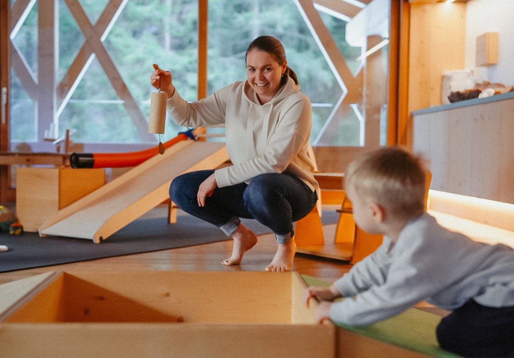 Saskia hebt ein Spielzeug in der Hand und zeigt es einem Kleinkind