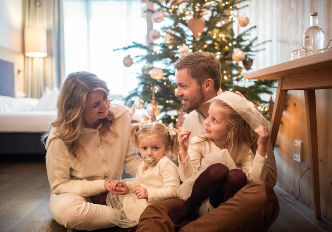 Familie sitzt vor Weihnachtsbaum im Zimmer