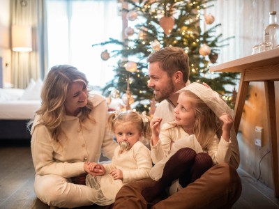Familie sitzt vor Weihnachtsbaum im Zimmer