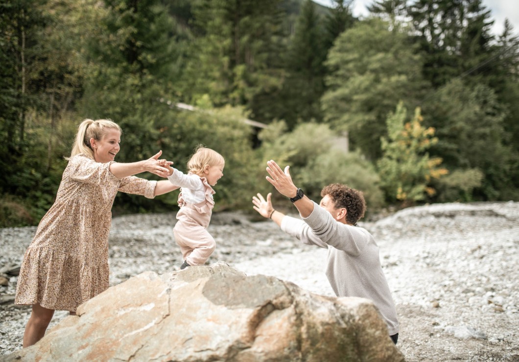 Kleinkind steht auf großem Stein und öffnet die Arme um Papa zu umarmen