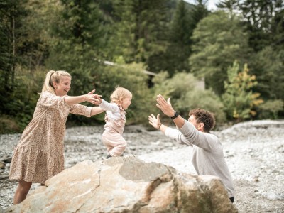 Kleinkind steht auf großem Stein und öffnet die Arme um Papa zu umarmen