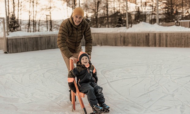 Ein Vater lernt mit seinem Sohn Eislaufen und schiebt ihn auf der Lernhilfe am Eis entlang.