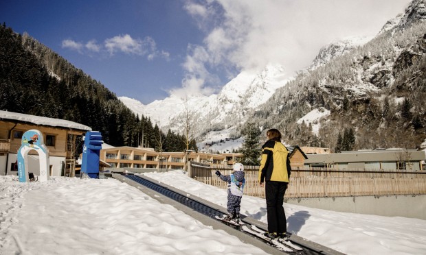 Ein Kind macht seine ersten Skiversuche im Feuerstein Garten und fährt mit der Skilehrerin mit dem Beförderungsband den Hügel hoch.
