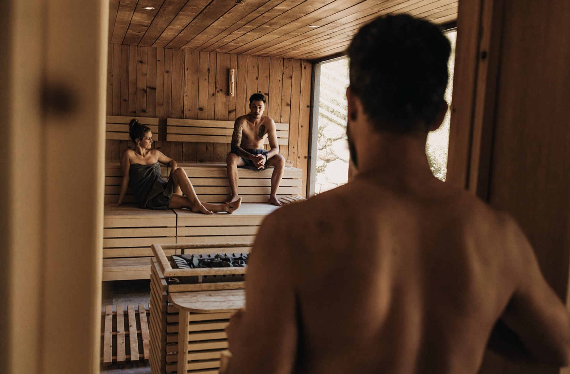 3 Personen sitzen in einer Sauna und ein anderer Mann betritt diese gerade