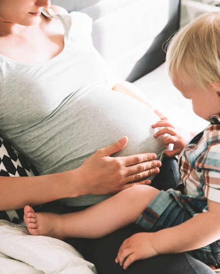 Kleiner Junge begutachtet den schwangeren Bauch seiner Mutter