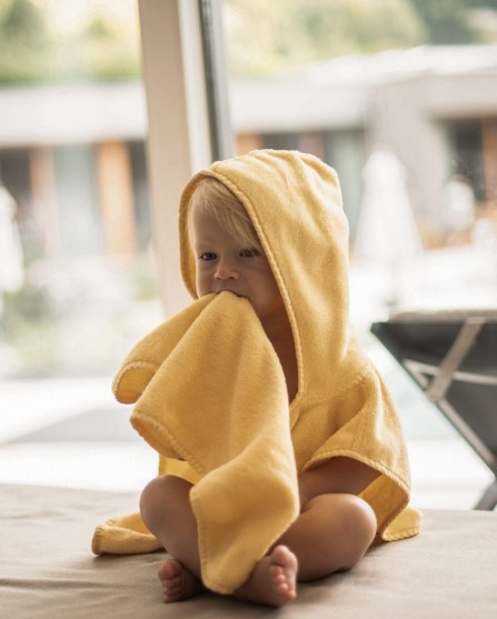 Kleines Kind sitzt mit einem gelben Bademantel