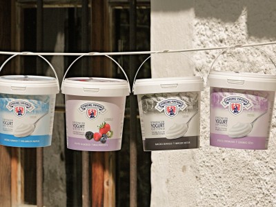 Drei Eimer mit frischer Milch und Joghurt hängen an einer Wäscheleine vor einer rustikalen Wand.