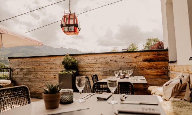 Eine gemütliche Bistro-Terrasse mit Blick auf eine Seilbahn und Berglandschaft.