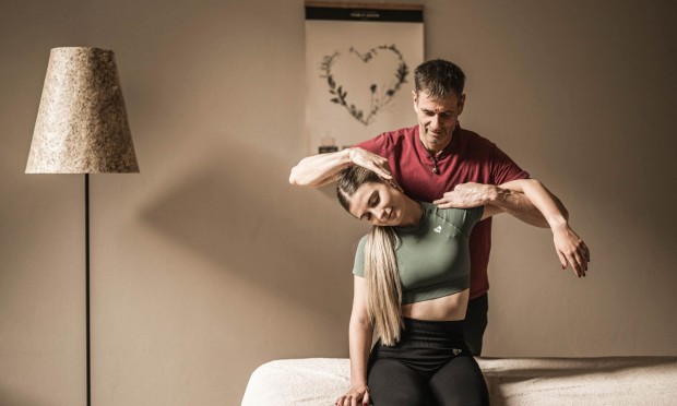 Ein Therapeut dehnt vorsichtig die Schultern eines sitzenden Patienten.