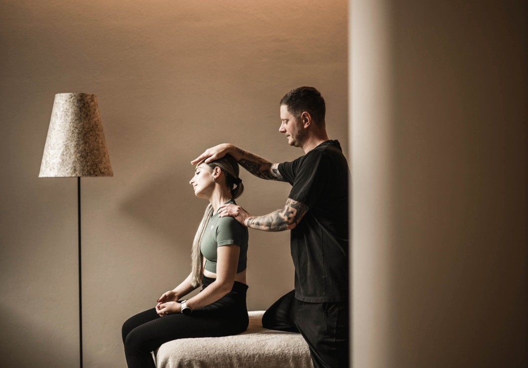 Ein Therapeut massiert den Nacken einer sitzenden Person in einer ruhigen Umgebung.