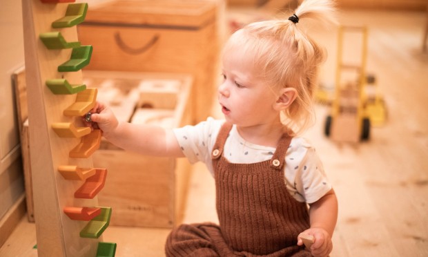 Ein Kleinkind spielt mit einer bunten Kugelbahn in einem liebevoll gestalteten Spielbereich.
