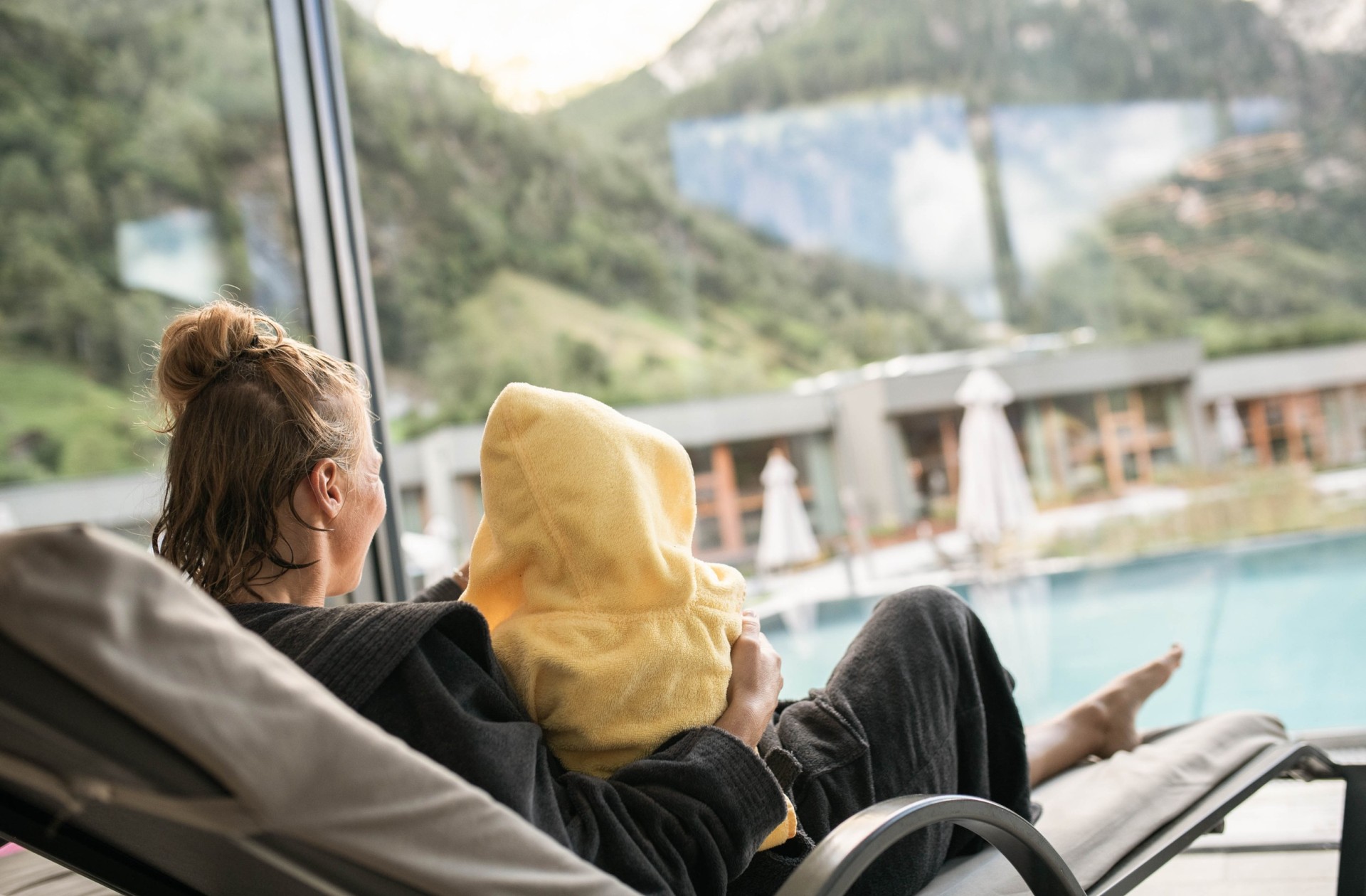 Mutter liegt im Bademantel auf einer Liege mit einem Kind, das einen gelben Bademantel angezogen hat