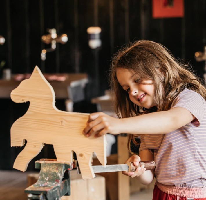 Kleines Mädchen raspelt ein Holzpferd in der Werkstatt