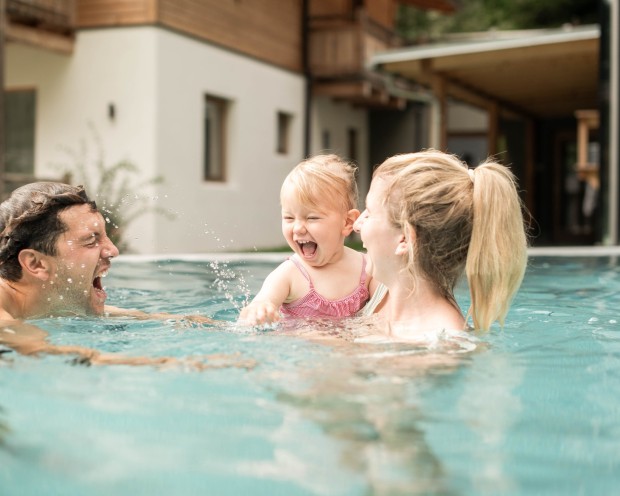 Vater und Mutter spielen mit Tochter im Wasser im Wellness Familienhotel Südtirols.