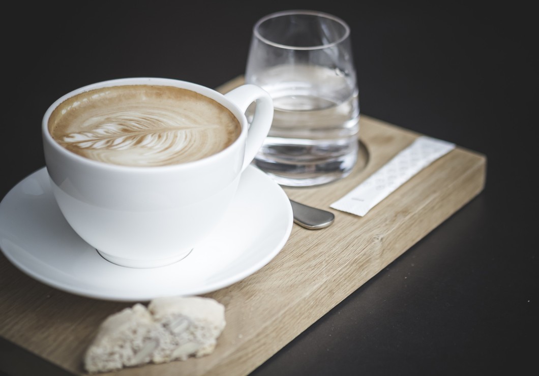 Eine Tasse Cappuccino mit einem Glas Wasser auf einem Holztablett.