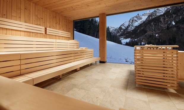Eine großzügige Sauna mit Panoramafenstern und Holzbänken, umgeben von Bergen.