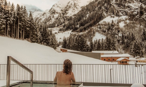 Eine Frau lehnt an einem Geländer und schaut auf eine verschneite Berglandschaft.