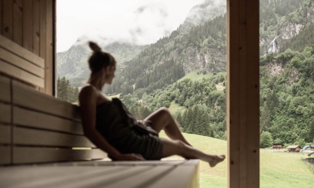 Eine Person entspannt auf einer Holzbank mit Blick auf die Berge.