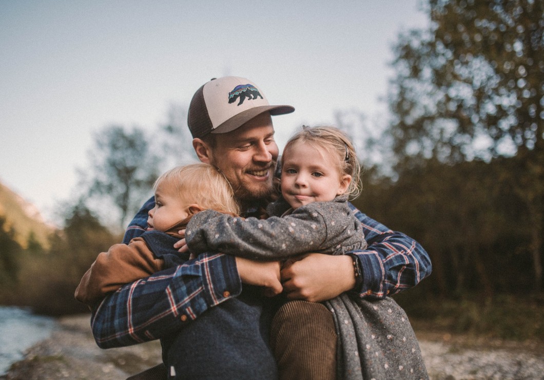 Ein Vater hat seine Kinder im Arm, neben dem Feuerstein am Bach
