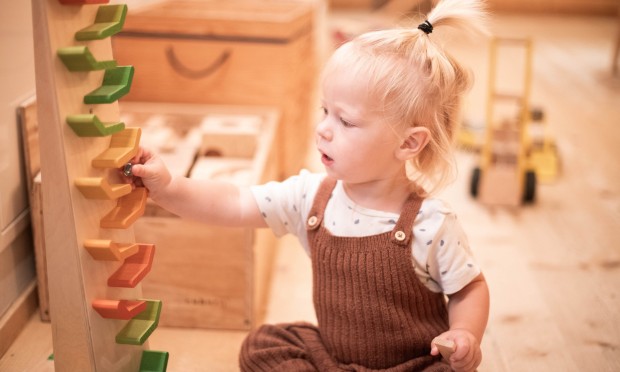 Ein kleines Mädchen spielt mit einer Montessori-Holzbahn in einem gemütlichen Raum.