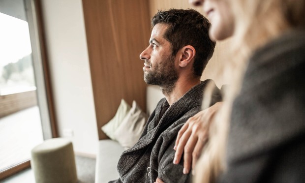 Ein Mann mit Bart hält eine Tasse Tee und blickt nachdenklich aus dem Fenster.