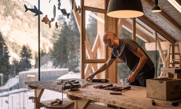 Ein Erwachsener und ein Kind arbeiten gemeinsam an einem Holzprojekt in einer Werkstatt mit Panoramafenstern.