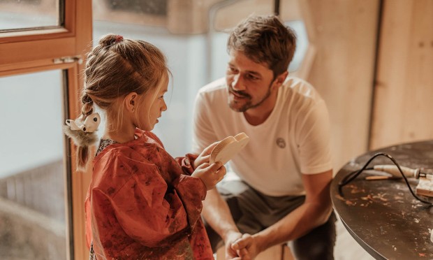 Ein Vater kniet vor seinem Kind und zeigt ihm liebevoll etwas in der Hand.