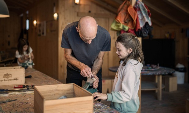 Werkstattmeister zeigt Kind wie man Holz abschleift