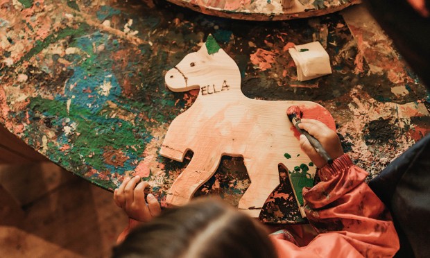 Ein Tisch voller Bastelmaterialien mit einem großen, bemalten Holzstück im Mittelpunkt.