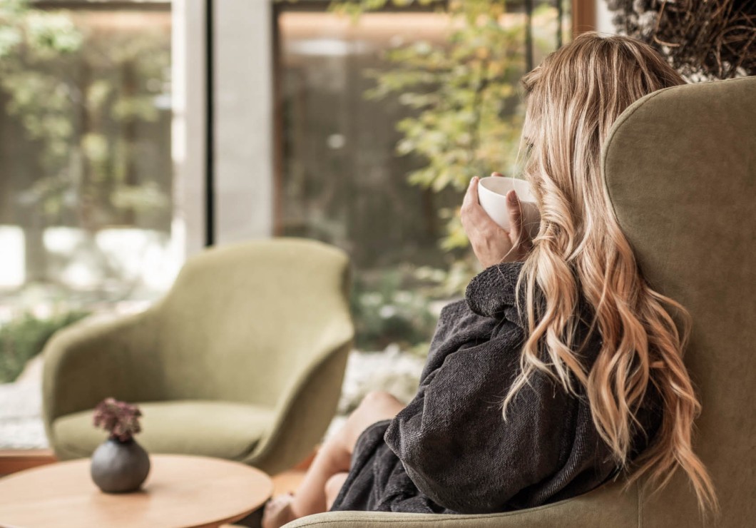 Frau sitzt im Sessel und trinkt einen Tee aus einer Tasse