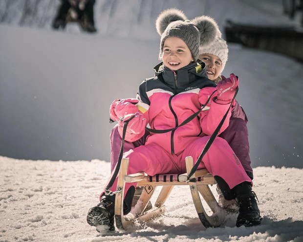 Kinder beim Schlittenfahren im Familienhotel Feuerstein in Südtirol