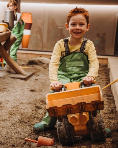 Junge sitzt auf Spielzeug Bagger im Matschraum