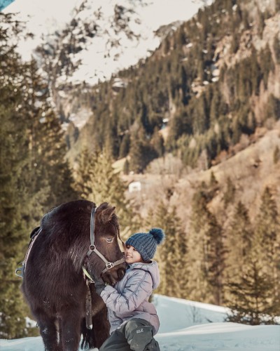 Kleines Mädchen kniet sich im Schnee nieder und streichelt ein Pony