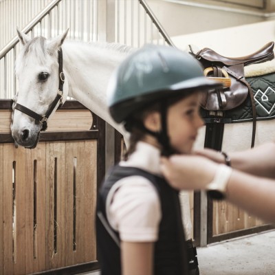 Reitlehrerin legt einem Kind einen Helm an