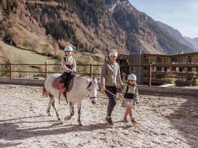 Reitlehrerin begleitet ein Kind, was wiederrum ein Pony mit einem Kind begleitet
