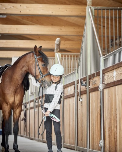 Kleines Kind steht neben ein Pferd im Reitstall