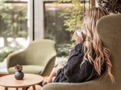 Frau sitzt im Sessel und trinkt ein heißes Getränk