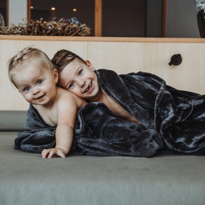 2 Kleinkinder liegen nebeneinander, eingewickelt in einer kuscheligen Decke