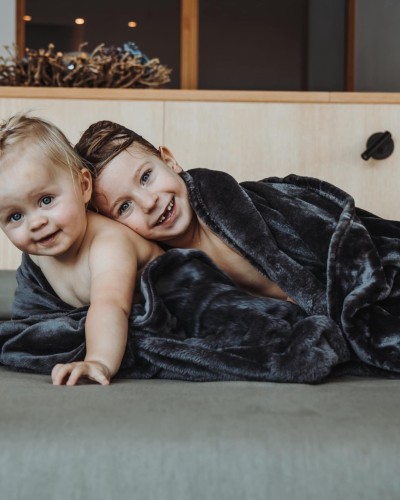 2 Kleinkinder liegen nebeneinander, eingewickelt in einer kuscheligen Decke