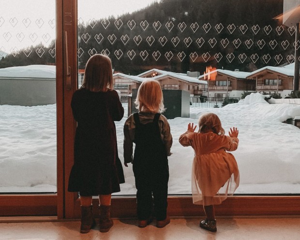 3 Kinder stehen bei einer Fensterscheibe und schauen nach außen