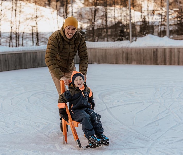 Kleiner Junge sitzt auf einem Stuhl auf dem Eisplatz, um Schlittschuhlaufen zu lernen