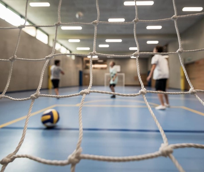 Fußballplatz in einer Halle und 3 spielenden Teenager