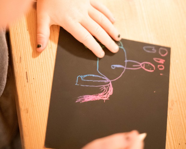 Ein Kind malt mit Ölfarben auf ein dunkles Papier.