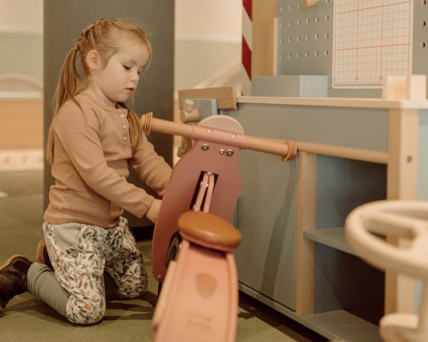 Ein kleines Kind fährt auf einem Holzroller in einem liebevoll gestalteten Spielbereich.